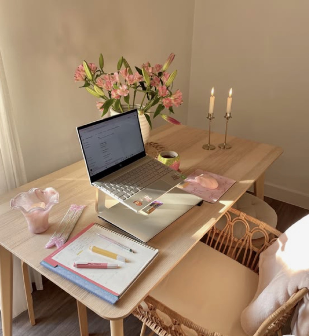 Mesa com computador, flores, cadernos e velas